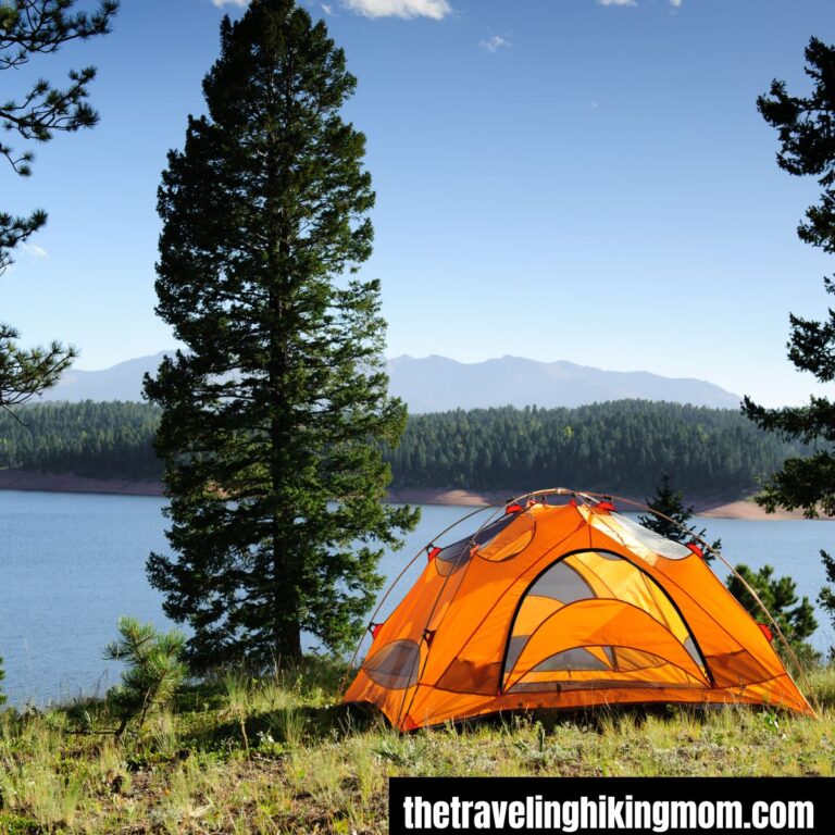 tent on a hill in front of a body of water surrounded by trees for camping on a budget