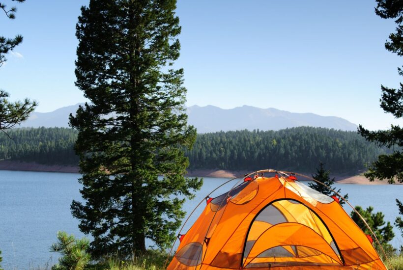 tent on a hill in front of a body of water surrounded by trees for camping on a budget